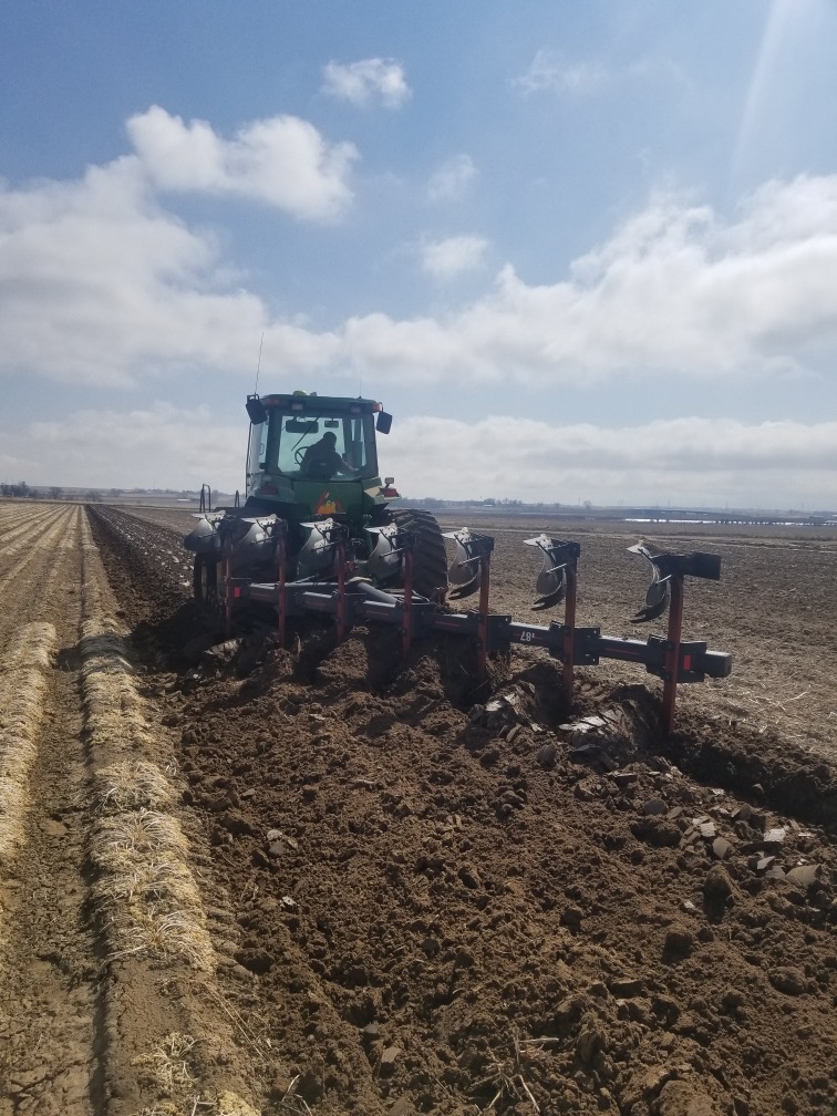 A tractor tilling soil in an empty lot of farmland.