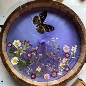 Round plate with purple resin design with embedded flowers and butterflies. 